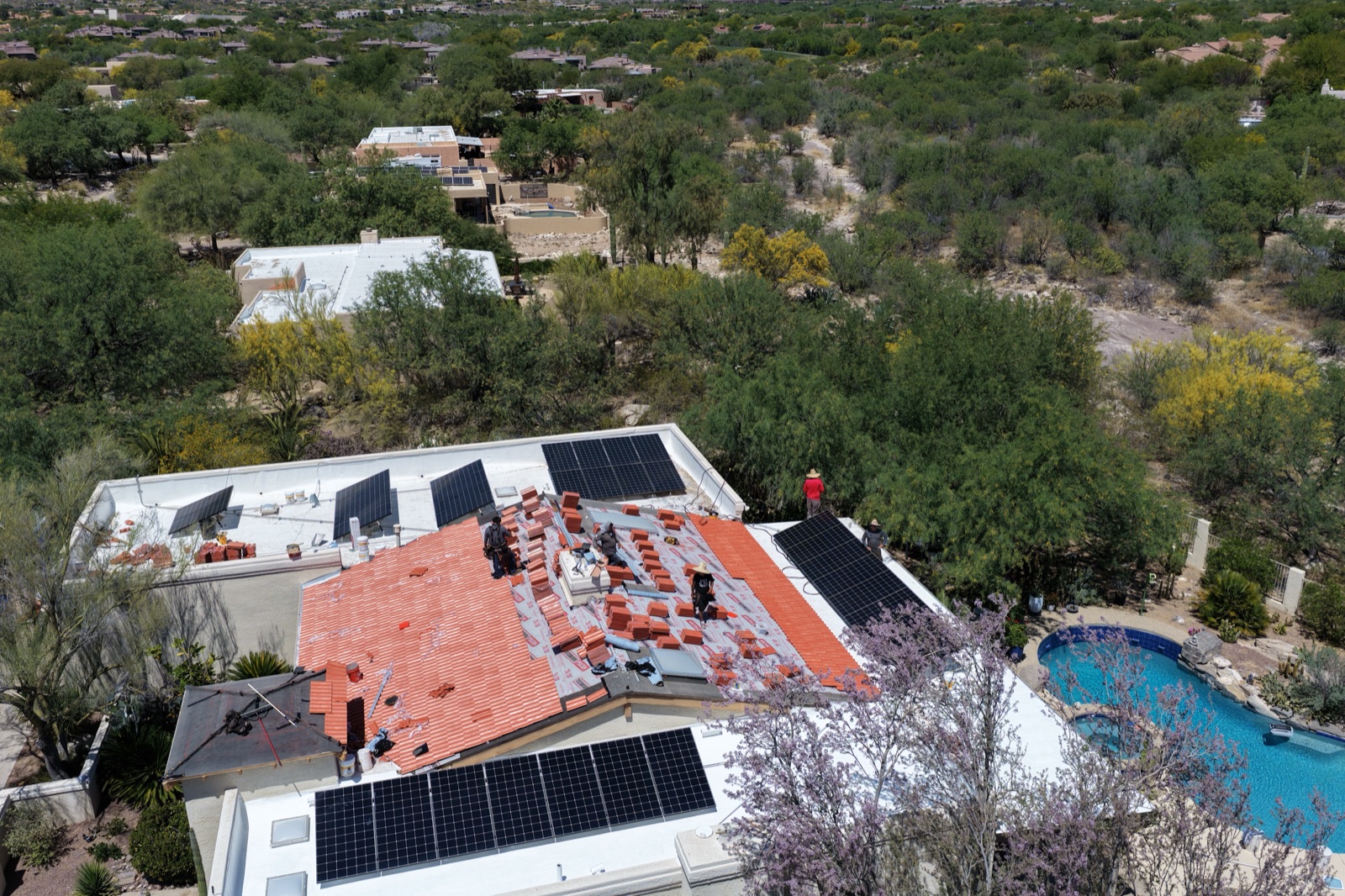 Drone photo of roofing crews working around solar panels during a tile re-roof
